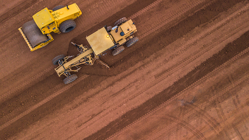 2 yellow construction machines digging up and flattening land