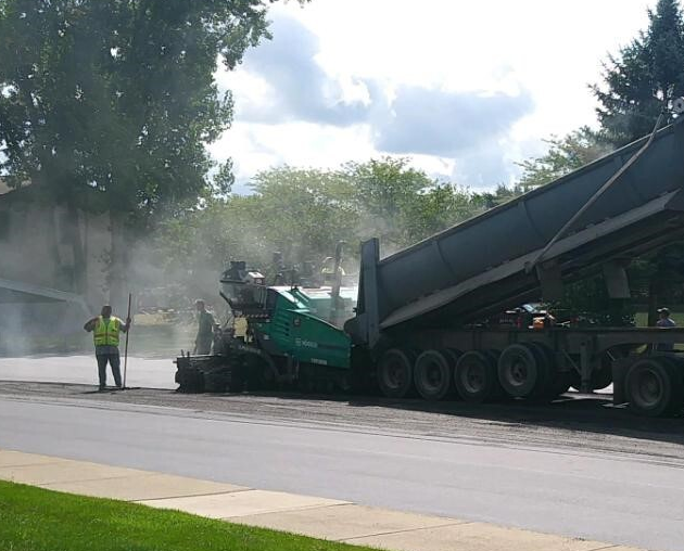 R&R Asphalt worker overseeing a truck paving the road