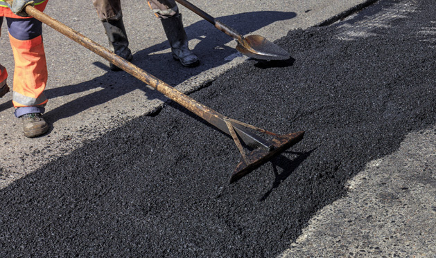 Someone smoothing out new asphalt with special rakes and shovels