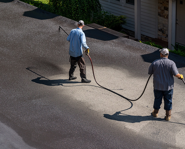 Two R&R asphalt workers sealcoating a driveway